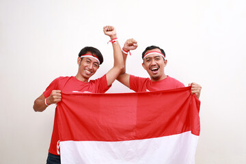 Two Indonesian men with a happy successful expression wearing red top and headband while holding...