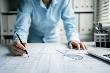 A women architect use pencil drawing draft on blueprints in the office, working with modern house blueprint floorplans, architectural and construction project concept.