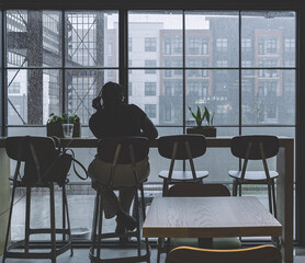 Woman thinking and working on a laptop in a coffee shop and looking through the window on a moody rainy day.