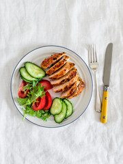 Delicious healthy lunch - baked chicken breast and fresh vegetables in a plate on a light background