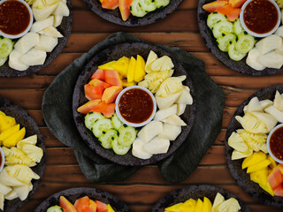 Indonesian fruit salad, also called lotis or rujak buah, on a wooden table. Lotis is a mixture of young fruits (jicama, mango, cucumber, papaya, pineapple) served with sweet and spicy peanut sauce.