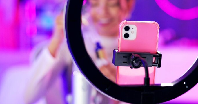 Phone, girl and ring light for live streaming with makeup or beauty tutorial for followers in neon room. Influencer, content creator and cellphone for skincare product review or sponsorship at home
