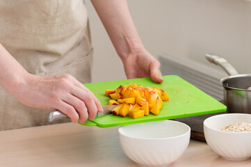 A woman adds chopped peach to her oatmeal.