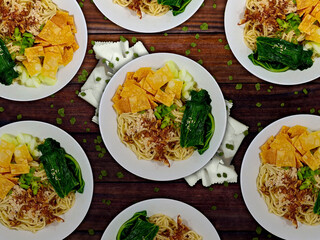 Indonesian chicken noodles on a wooden table. Flay lat view. Indonesian called it mie ayam, influenced by Chinese food. Savory chicken noodle with green Choy Sum, fried dumpling skin and shallots.