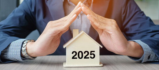 Businessman hands over wooden House model with 2025 New Year text. Property insurance and real...