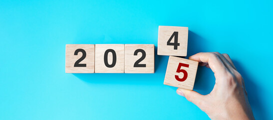 hand holding wooden cube block with 2025 text on blue background. Resolution, plan, review, goal,...