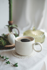 a cup of coffee and a vase with a plant in the background
