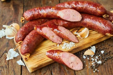 The sausage lies on a wooden surface surrounded by vegetables. Meat production.