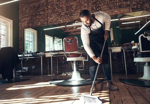 Barber, salon and man with broom for cleaning after grooming, shaving and hair cut for beauty service. Hygiene, workplace and hairdresser in barbershop sweeping for dirt, dust and mess on floor