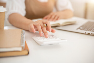 A close-up image of a woman using a calculator, working at a desk indoor.