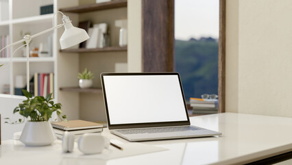 Fototapeta premium A close-up image of a laptop computer with a white-screen mockup on a white table in a modern room.