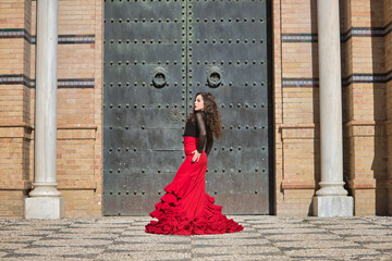 Young, beautiful, brunette woman in black shirt and red skirt, dancing flamenco in front of an old, black metal door. Flamenco concept, dance, art, typical Spanish.