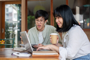 Fototapeta premium Young Asian man is working remotely with his colleague at a cafe, discussing work and brainstorming.