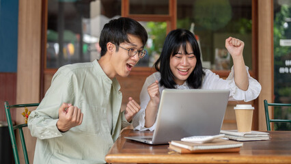 Two cheerful Asian friends, male and female, are sitting at a cafe, celebrating good news together.
