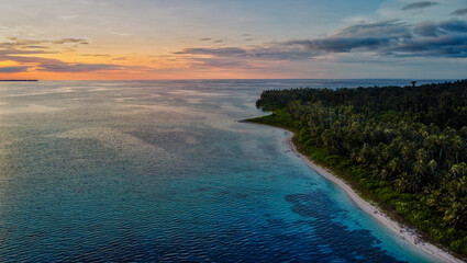 An aerial view of Sumatra's coastline during Sunset, showcasing the stunning contrast between lush tropical forests and vibrant turquoise waters. A paradise waiting to be explored.