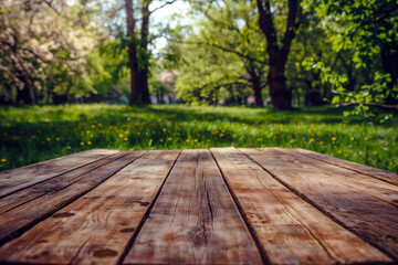 Empty wooden tabletop standing on a blurred green meadow background on a sunny day