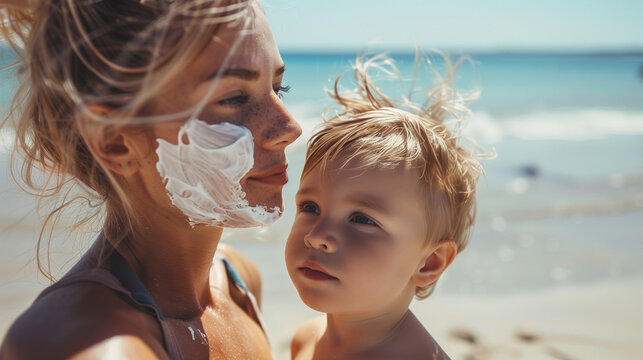 A mother and her little son have white sunscreen on their faces. They stand together on the beach, where they protect themselves from the harmful effects of the sun.
