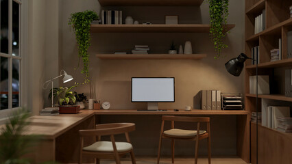 A cozy contemporary home workspace at night features a computer on a wooden L-shaped table. © bongkarn