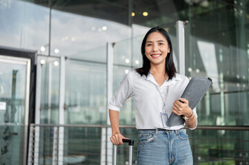 An attractive Asian female passenger with her luggage is standing at the exit door of the airport.