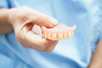 Asian senior woman patient holding teeth denture in her hand for chew food.