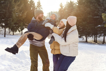 Portrait of happy smiling young family with son and daughter standing outdoors enjoying time together in winter forest. Mother, father with two kids walking outside. Family leisure concept.