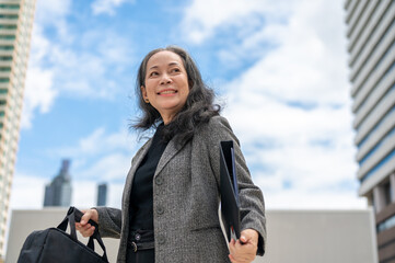 Confident Asian senior businesswoman stands in the big urban city, commuting to work in the morning.