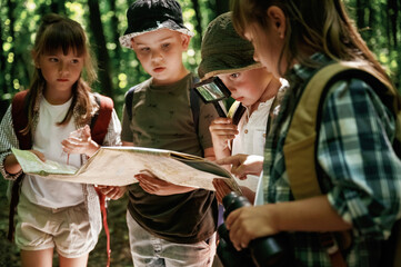 Looking at the map. Kids in forest at summer daytime together
