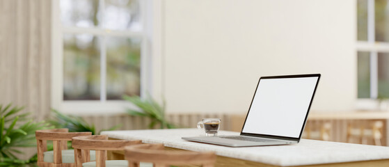 A laptop computer with a white-screen mockup on a table in a comfortable minimalist cafe.