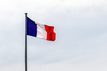 French flag blowing in the wind, on a metal pole, against clear grey sky, providing copy space.