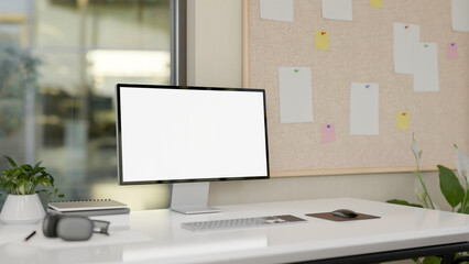 A computer desk in a modern office, a computer with a white-screen mockup on the desk.