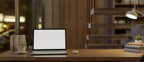 A laptop computer with a white-screen mockup on a wooden table in a modern home at night.