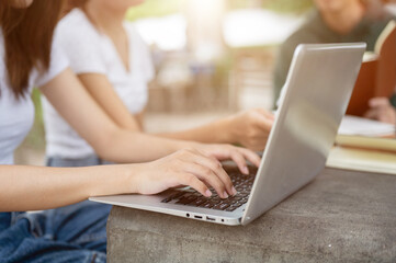 A female college student working on her laptop computer while studying with her friends outdoors.