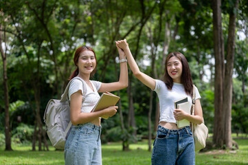 Obraz premium Two lovely Asian female college friends are in the park, holding hands and smiling at the camera.