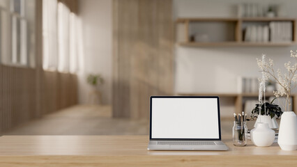 A laptop computer mockup and accessories on a wooden tabletop in a Scandinavian minimalist room.