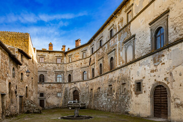 Fototapeta premium A glimpse of the ancient medieval village of Montecalvello, Viterbo, Italy. The internal courtyard of the castle with the ancient stone and brick buildings and the fountain in the center.