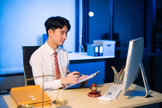 Young Asian lawyer at desk with legal scales and gavel, writing documents in office, offering legal services