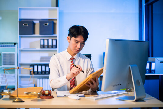 Young Asian lawyer at desk with legal scales and gavel, writing documents in office, offering legal services