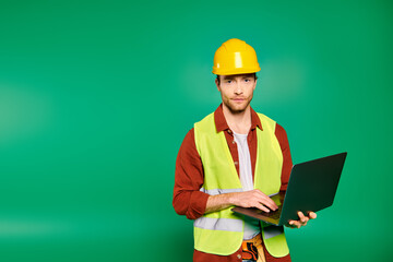 A man in a yellow safety vest holds a laptop.