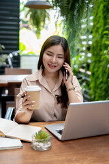 A businesswoman is talking on the phone and having a coffee while working remotely from a cafe.