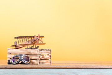 Toy plane and vintage goggles on old wooden table front yellow background. Retro style filtered photo