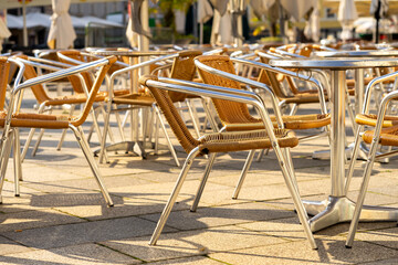 Many wicker chairs at cafe tables in the morning sun