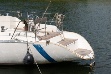 The rear deck of a sleek white sailboat docked at the marina, featuring clean lines and nautical...