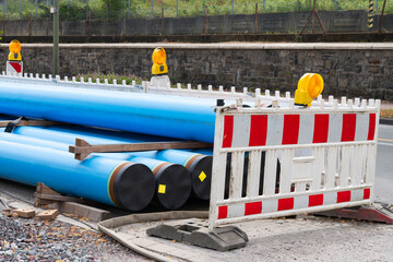 Blue water pipes laying in the street at a new construction site with white and red traffic fences...