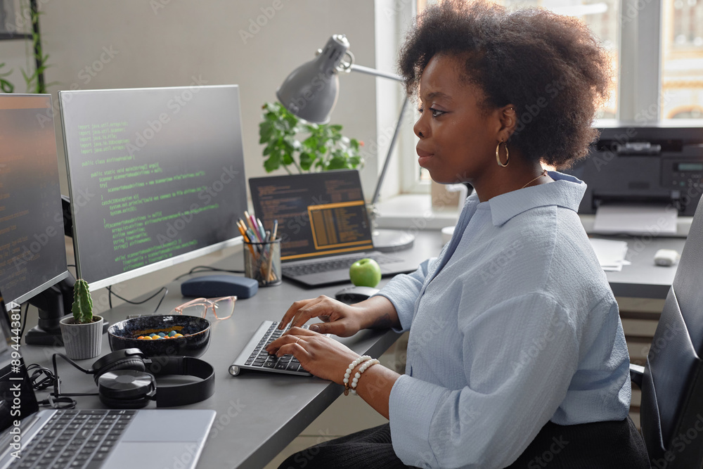 Poster side view of young african american female software developer using computer writing code while sitt