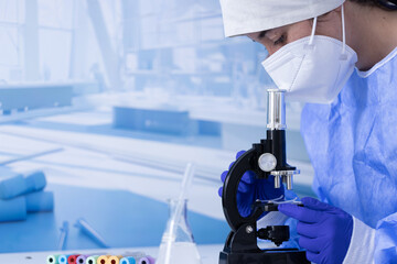 A woman wearing a white lab coat and a mask is looking through a microscope. The image is a close-up of the microscope and the woman's face