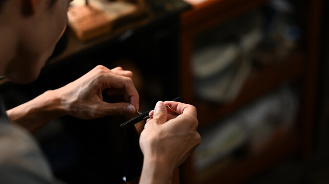 Young leather craftsman carefully stitching leather pieces. Small business and handmade concept