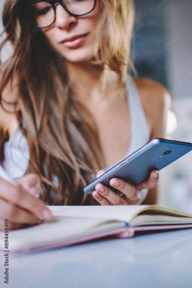 Poster cropped view of smart young woman writing down information in notepad from internet website doing ho