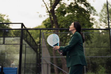A businesswoman in a green suit enjoying a game of padel tennis on an outdoor court surrounded by...