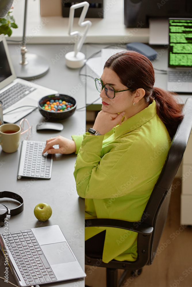 Poster vertical shot of thoughtful female senior it specialist reading computer screen while typing script 