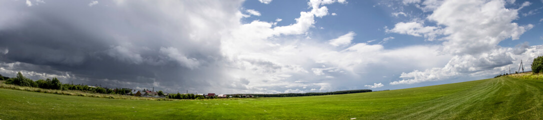 Panoramic view of green field with blue sky and white clouds